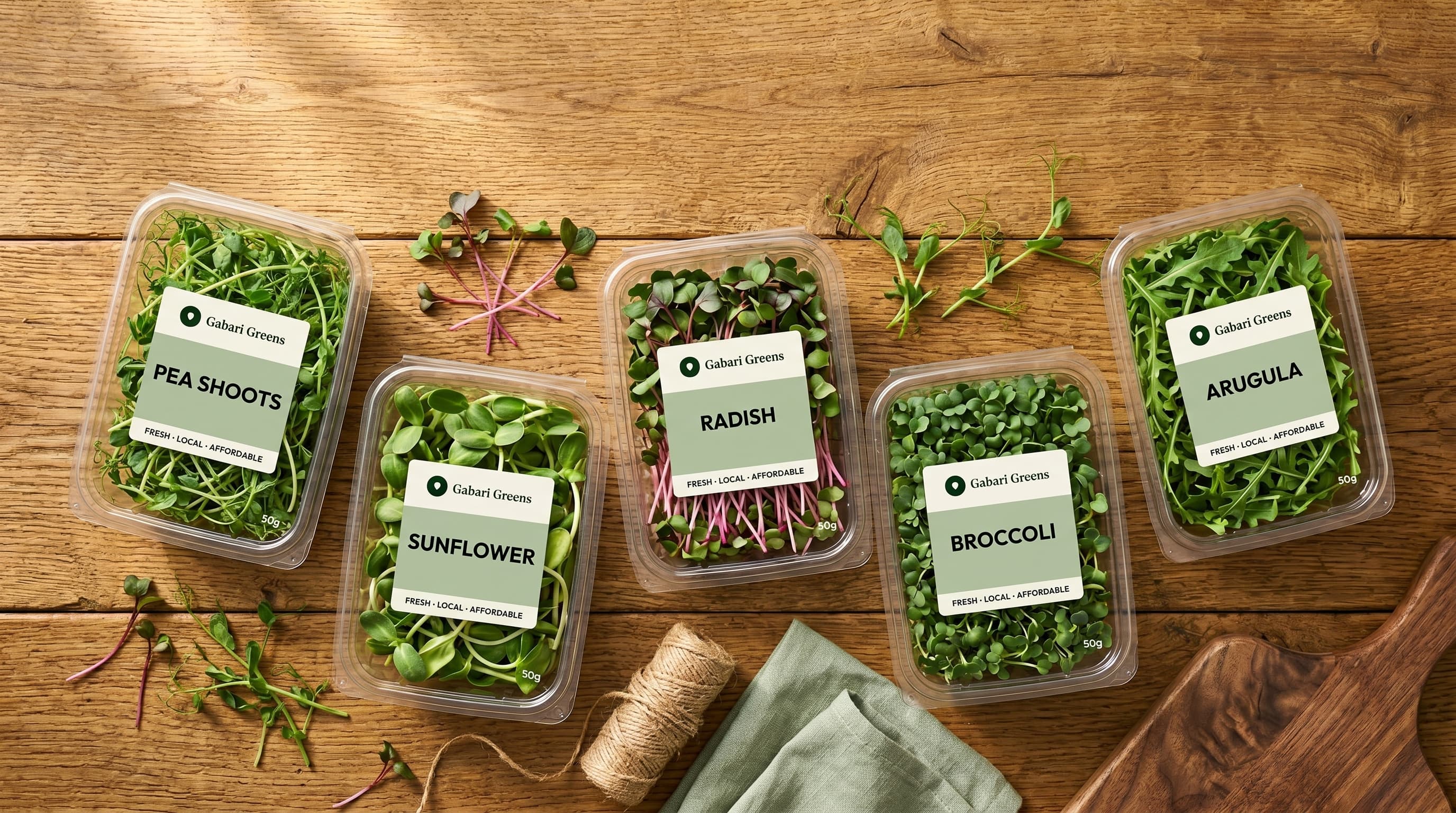 All five Gabari Greens varieties — pea shoots, sunflower, radish, broccoli, and arugula — in labelled clamshells on a wood surface